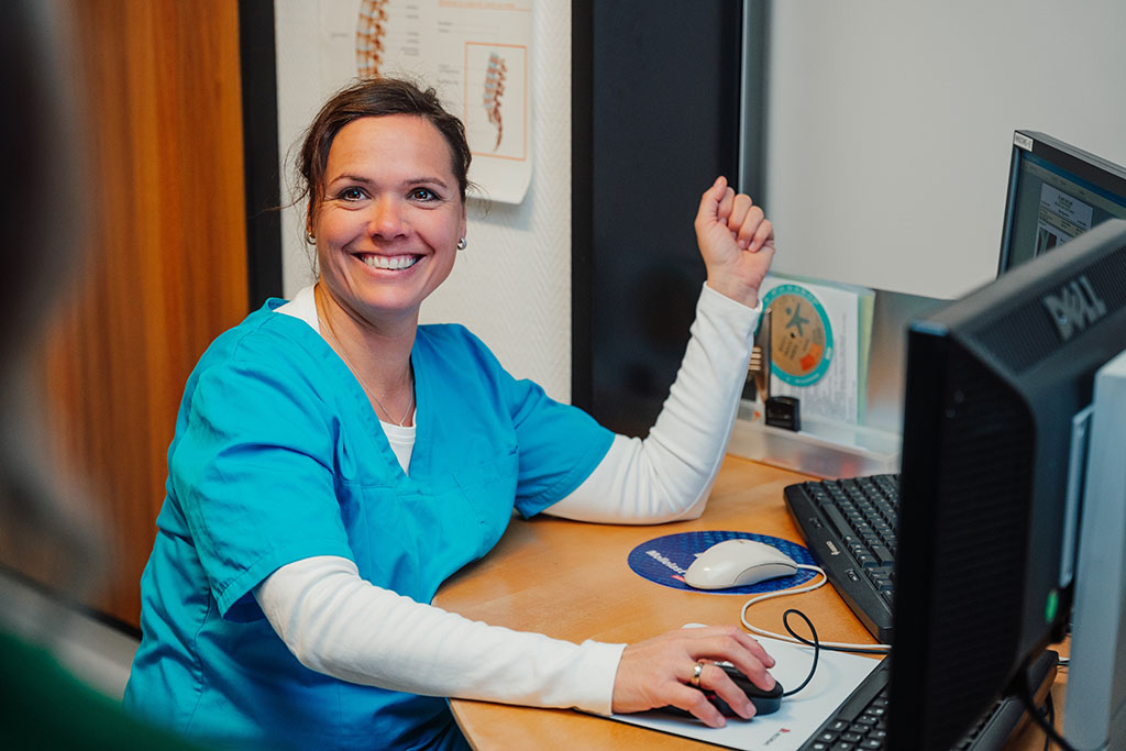 Medizinischer Fachangestelte sitzend am V+Computer am Empfang der Praxis für Orthopädie Dr. Gero Lenk in Sonthofen.